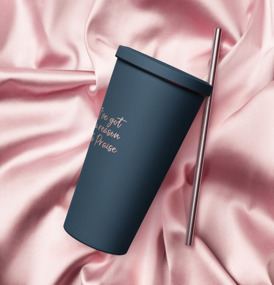 A navy-colored stainless steel insulated tumbler with a straw, featuring a text design on the side, placed on a pink, velvety surface.