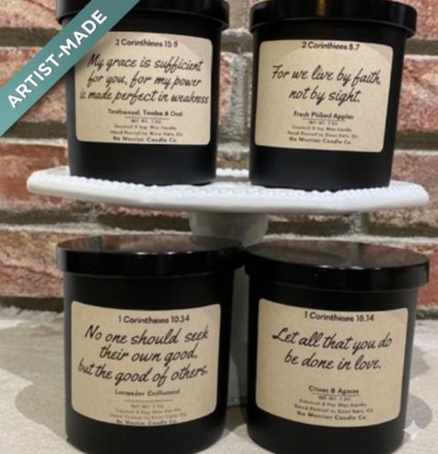 Four black candles with white labels on a white stand against a brick wall.