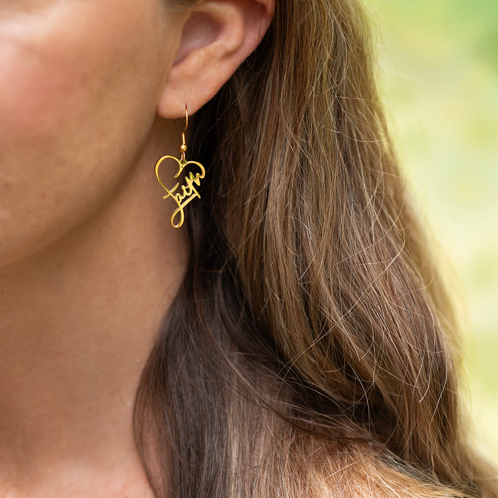 Gold heart-shaped earrings with 'love' inscription worn by a person with blurred background