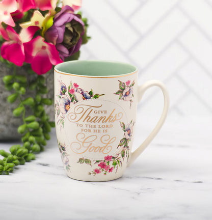 Decorative mug with floral designs and text, placed on a surface with flowers in the background.