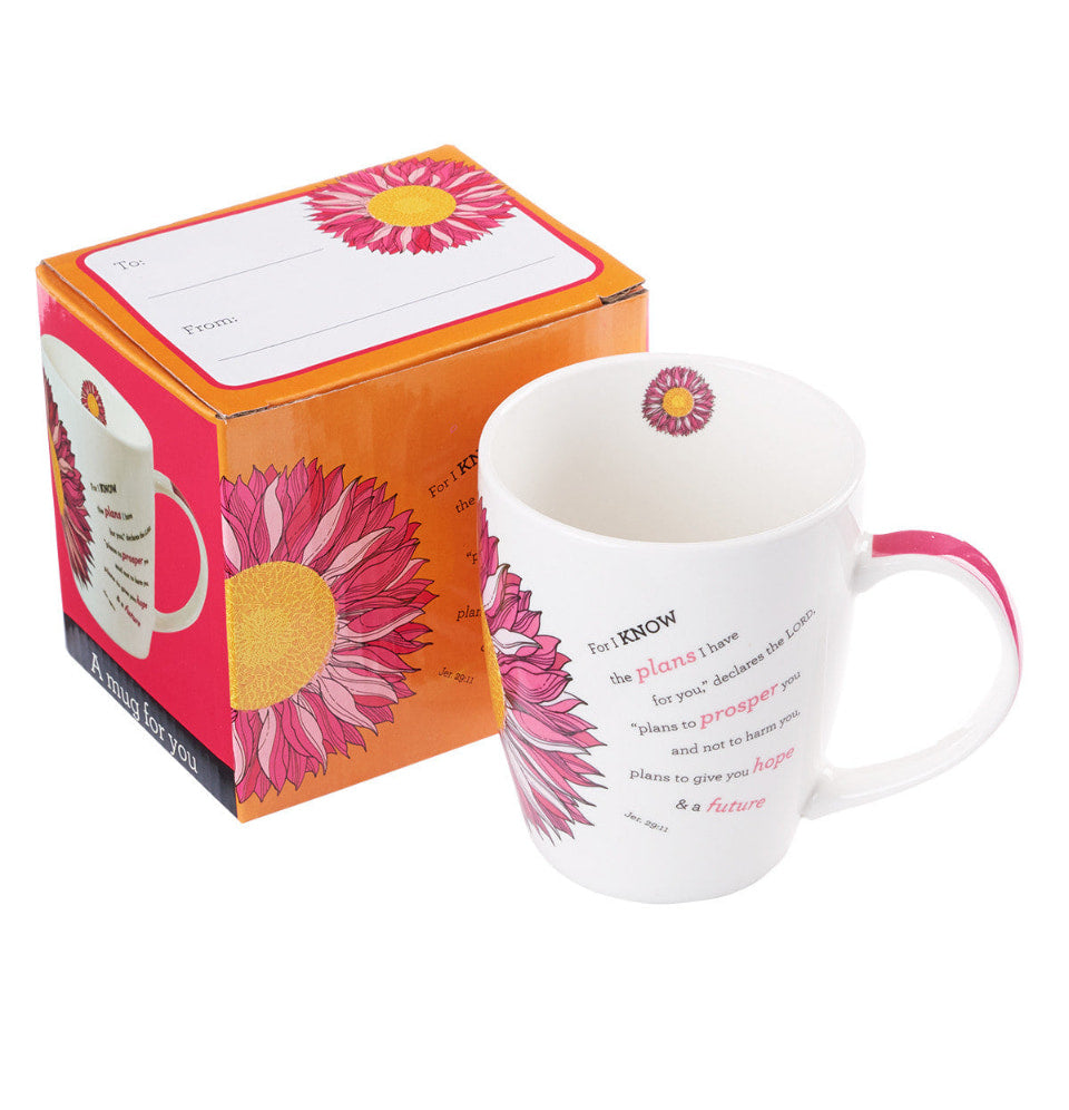 White mug with pink floral design and text, next to its packaging box on a white background
