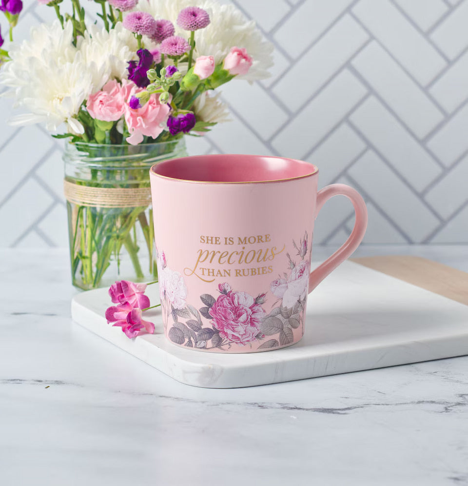 Pink mug with floral design and text, placed on a marble surface with flowers in the background.