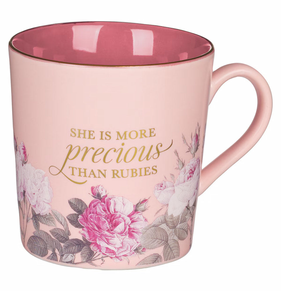 Pink mug with floral design and text 'She is more precious than rubies' on a white background