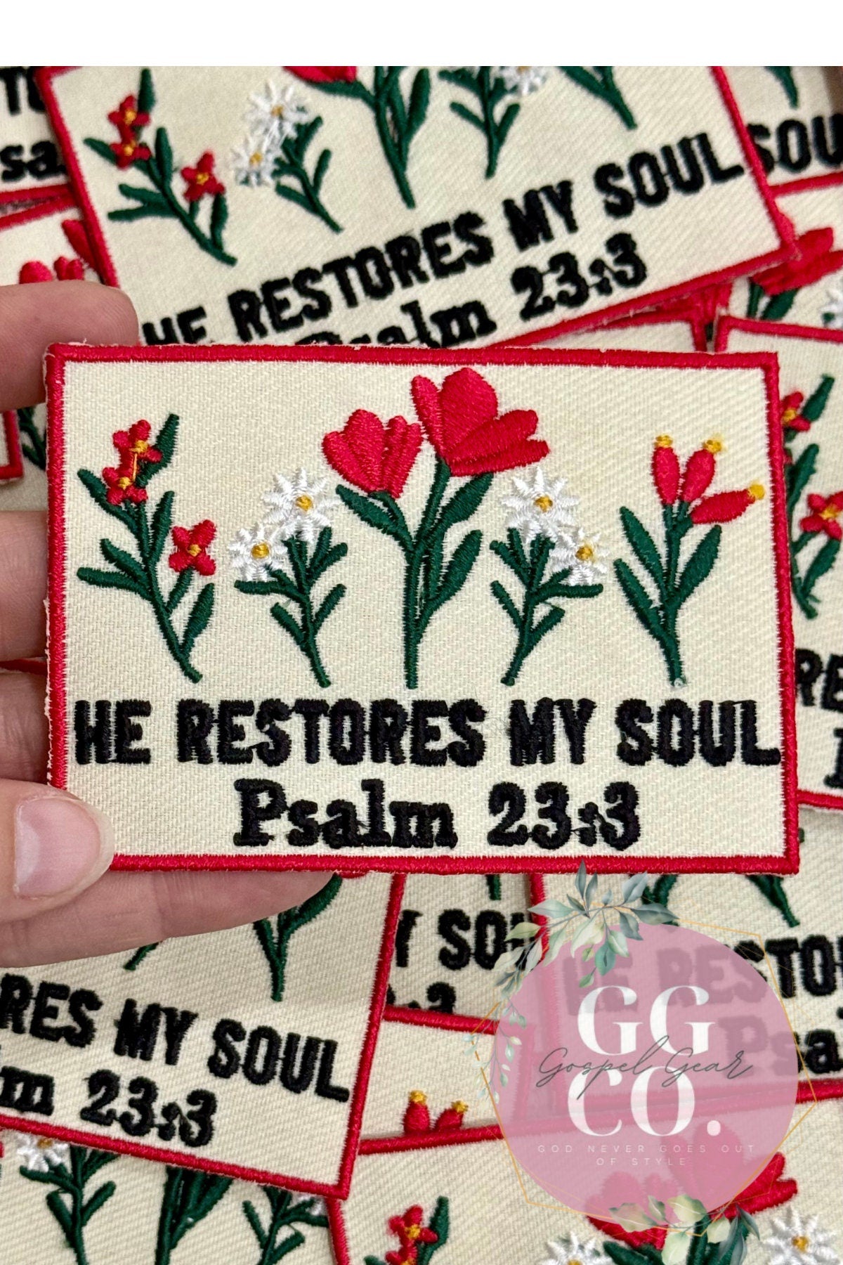 Embroidered patch with floral design and text 'He restores my soul Psalm 23:3' held by a hand.