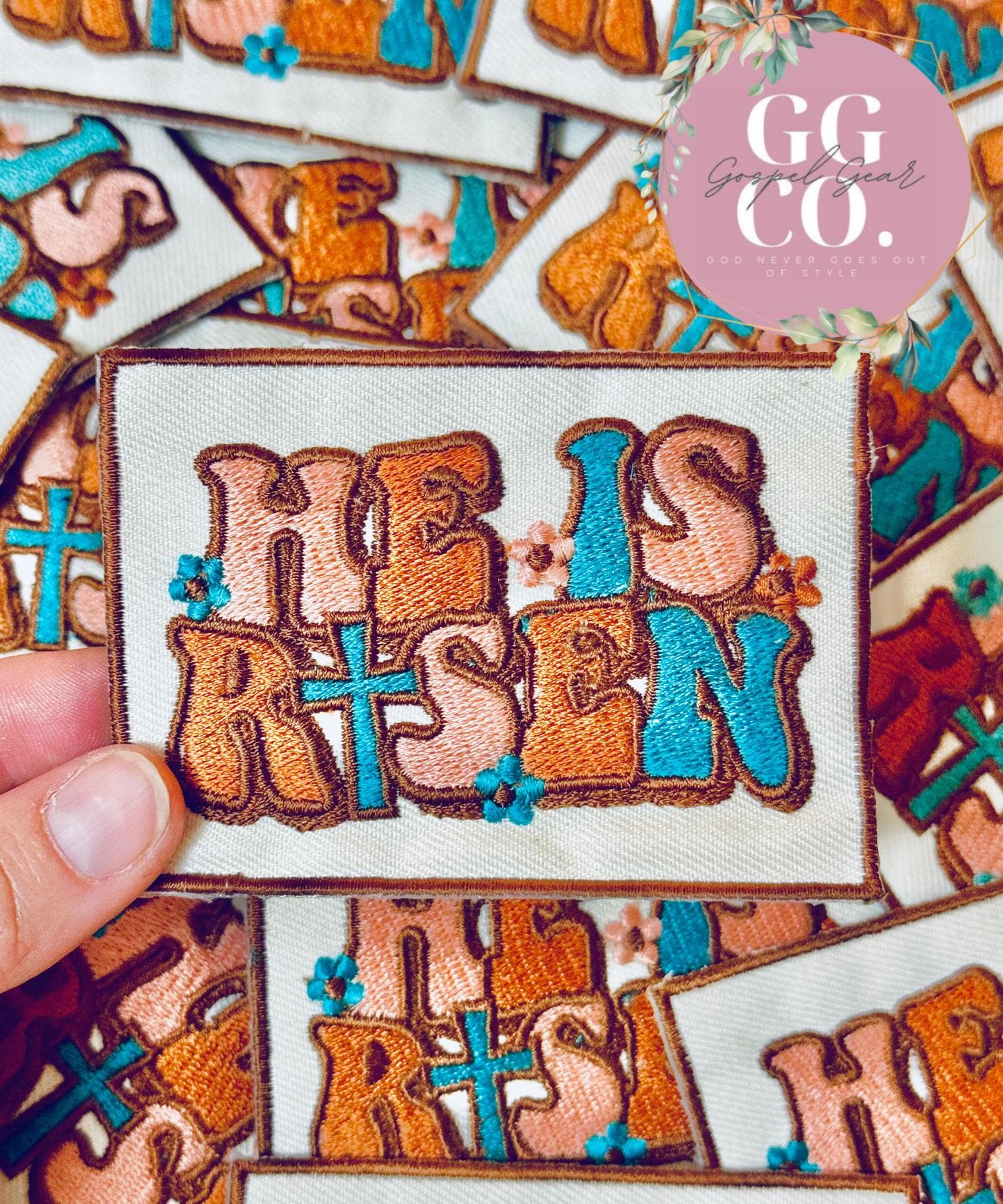 Embroidered patch with 'He is Risen' text held by a hand, with 'GG Co.' branding in the corner.