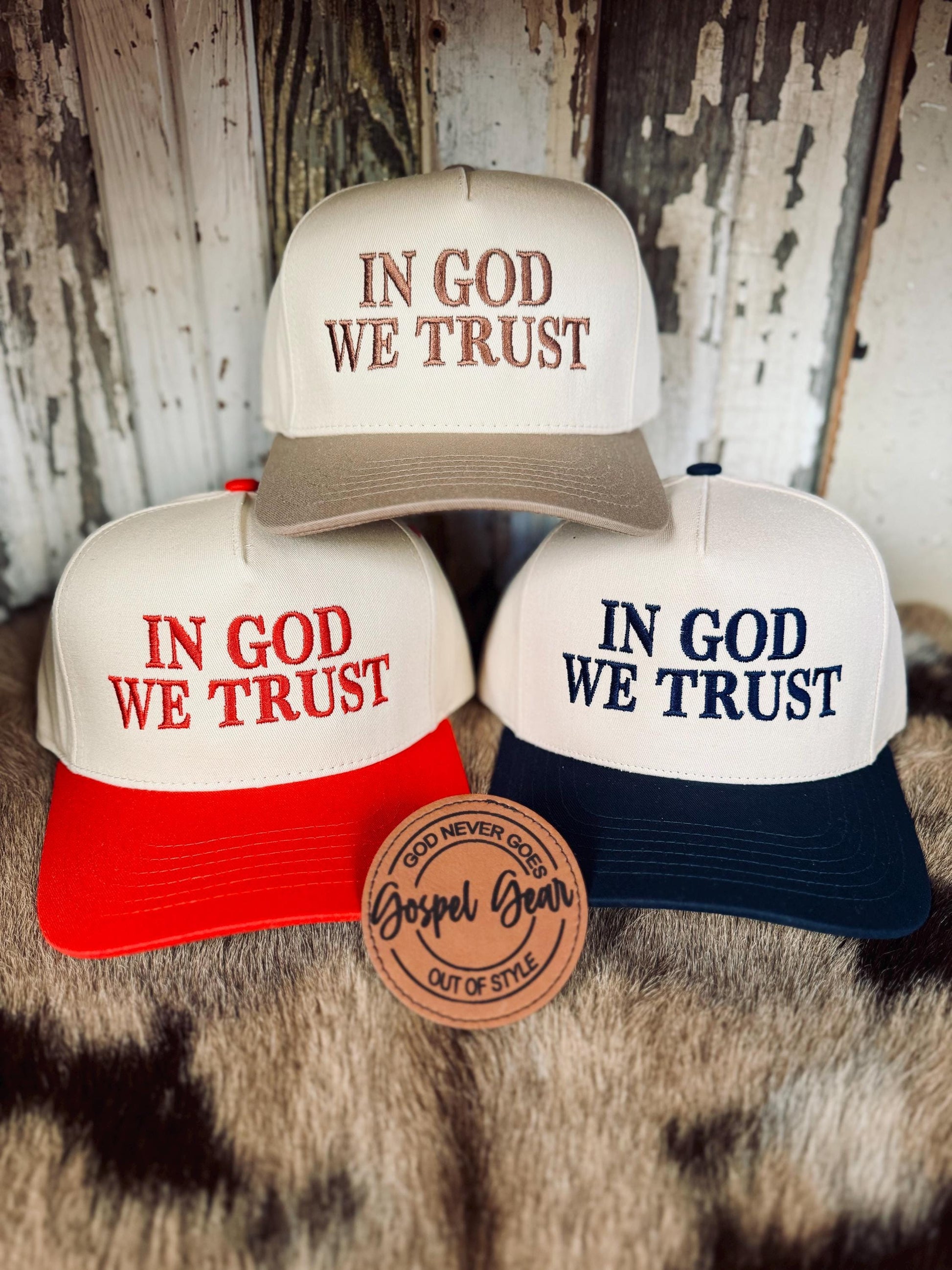 Three 'In God We Trust' hats in different colors on a rustic background