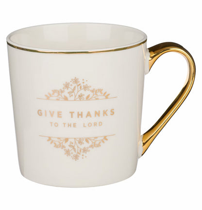 A white ceramic coffee mug with gold trim and floral design, handle facing to the side, with the text 'GIVE THANKS TO THE LORD' on the front.